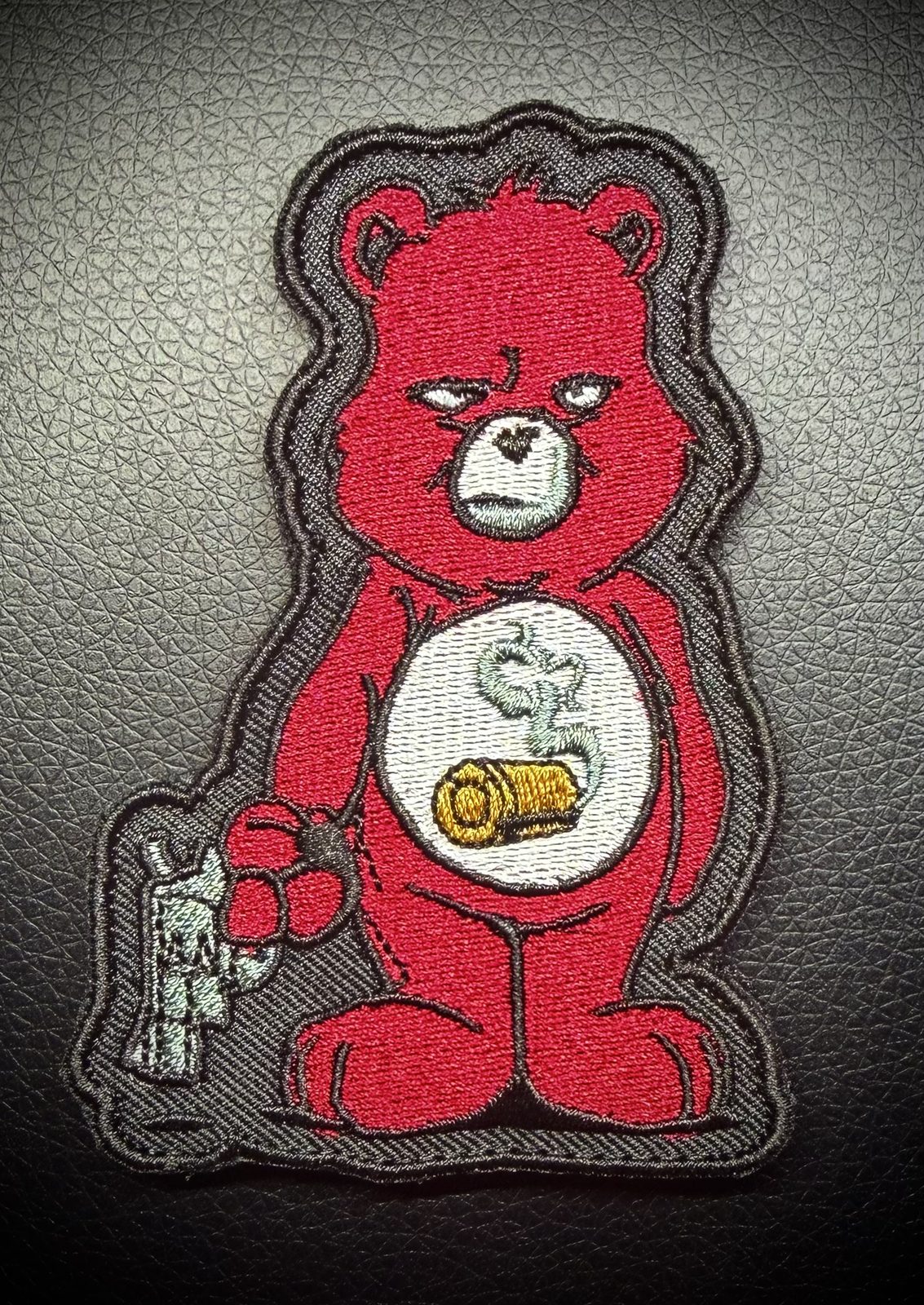 Grumpy red bear character morale patch holding a revolver with a bullet on its belly